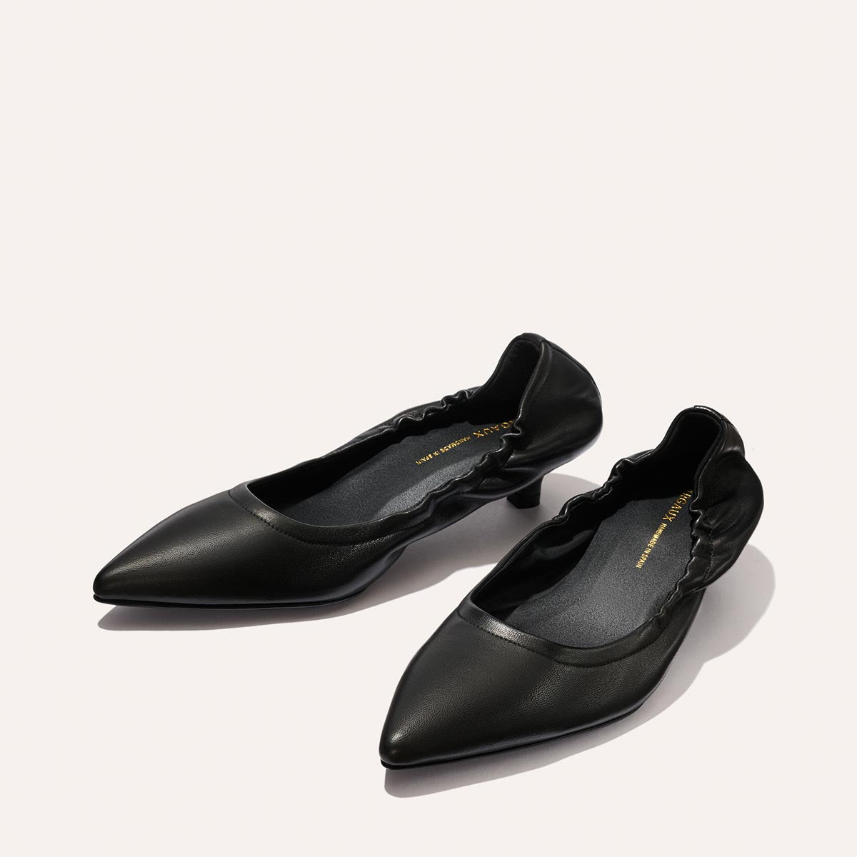 A pair of Margaux The Roma 40 - Black Nappa pointed-toe flats with ruched detailing around the opening, set against a light, neutral background.