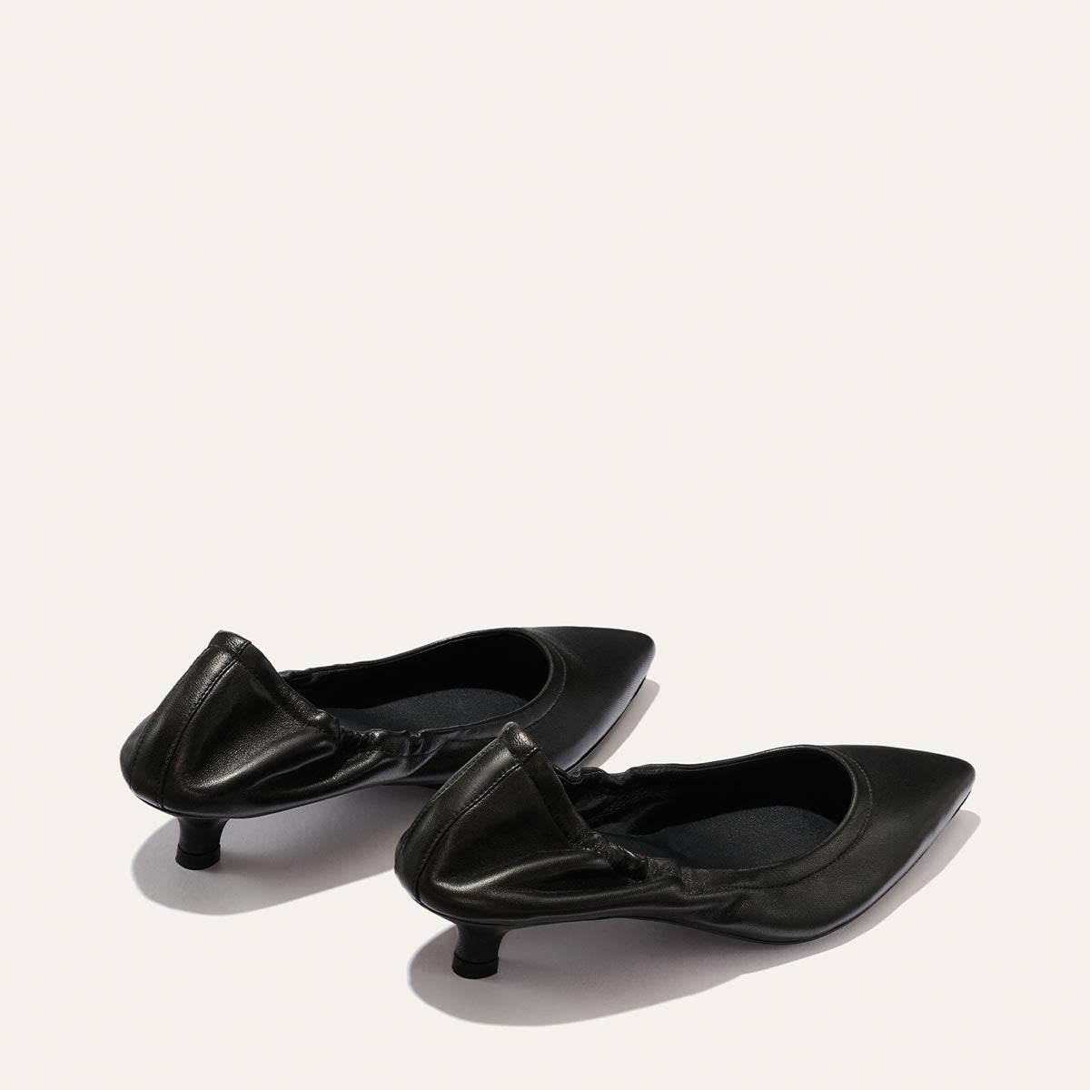 The Roma 40 - Black Nappa by Margaux: a pair of black chic kitten heels with ruched back detailing, displayed on a light background and positioned slightly apart.