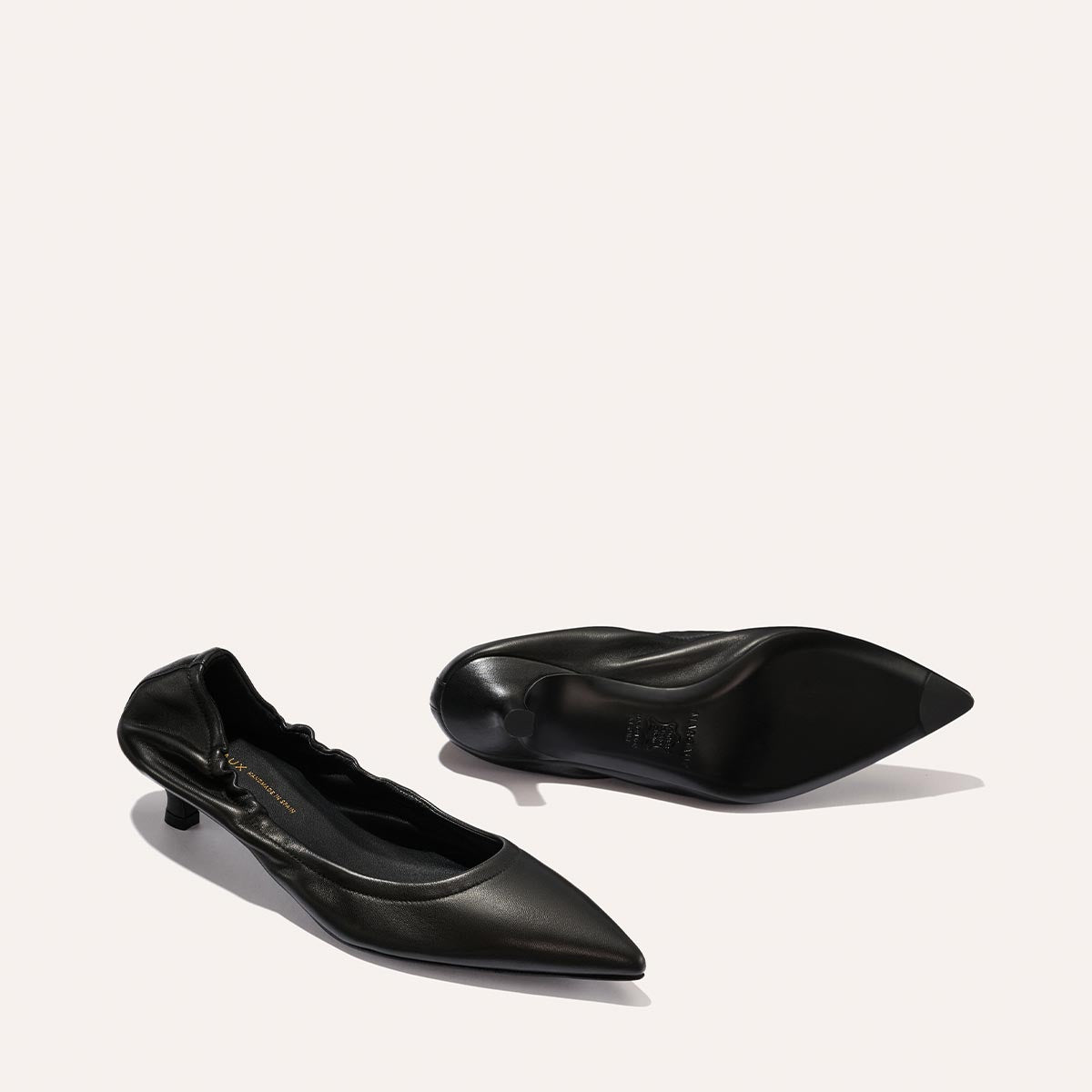 A pair of Margaux’s The Roma 40 - Black Nappa heels: one stands upright to show the sleek pointed toe and side, while the other lies on its side to reveal the sole, all against a plain light background.