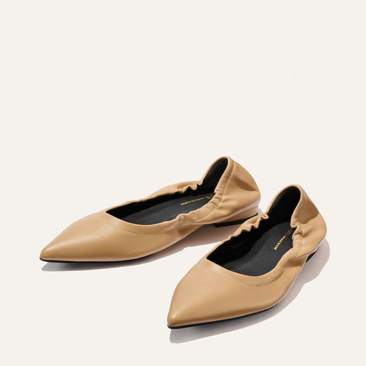 The Roma - Praline Nappa flats by Margaux feature a tan pointed toe, ruched edges, and black insoles, shown on a plain light background.