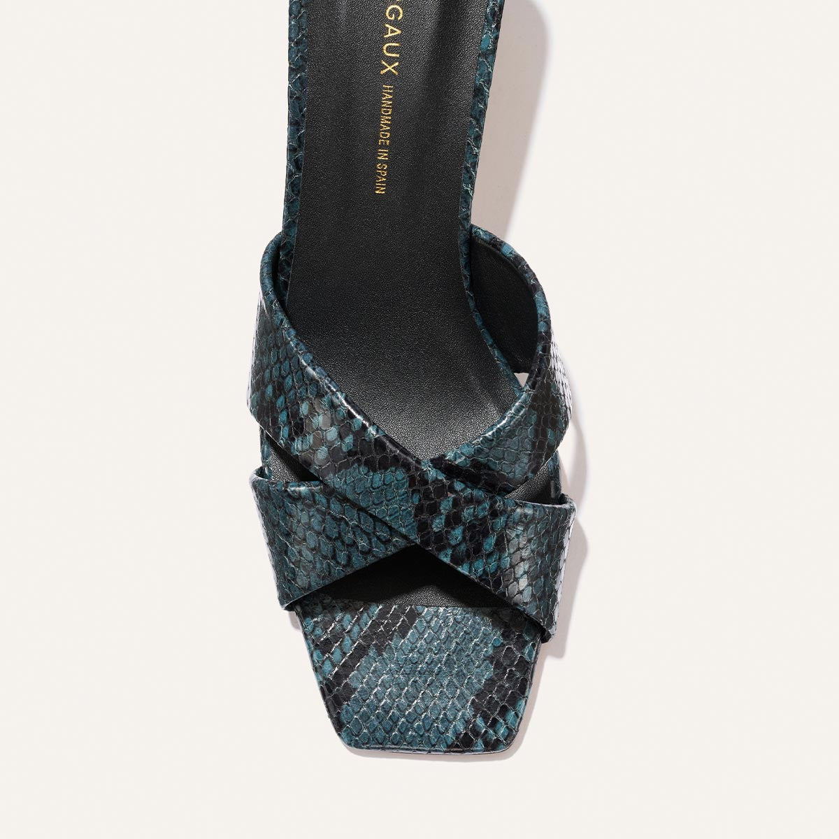 A close-up top view of Margaux’s The Selene 50 - Aqua Python Embossed sandal, featuring a square toe, blue and black python-textured crisscross straps, and a black insole with gold text.