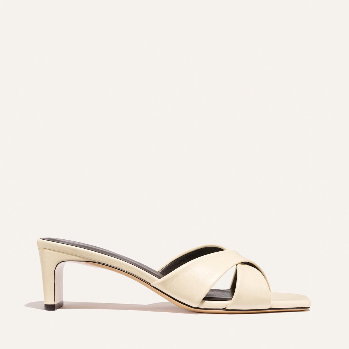 The Margaux Selene 50 - Ivoire Nappa is a cream-colored heeled sandal featuring crisscross leather straps, an open toe, and a mid-height heel, shown against a plain light background.