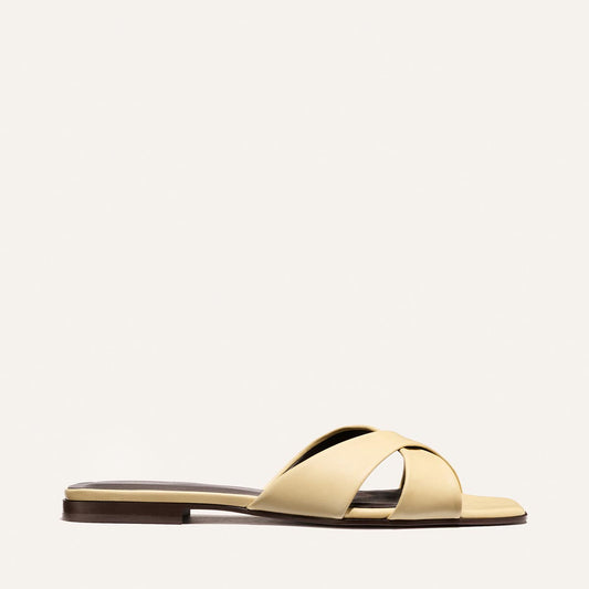 The Alex Mill x Margaux Selene Flat Sandal in Butter Nappa by Margaux features wide crisscross straps and an open toe—an effortless summer slip-on showcased on a plain light background.