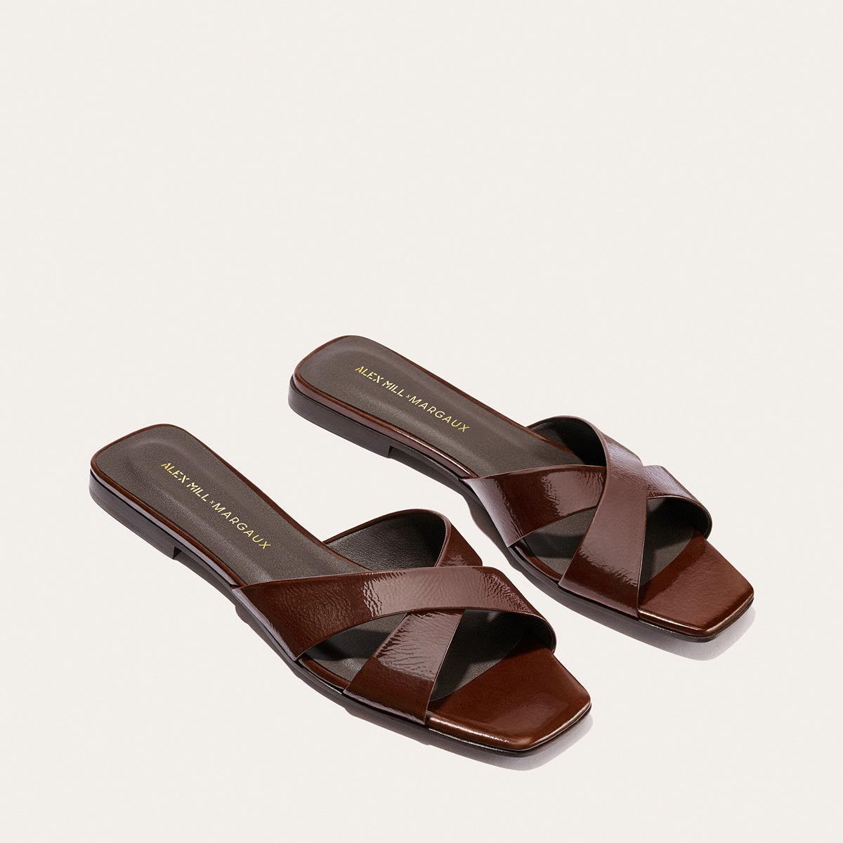 The Margaux Alex Mill x Margaux Selene Flat Sandal in Espresso Crinkle Patent features glossy crisscross straps, flat soles, and a stylish square toe—an ideal pick for your go-to summer sandal.