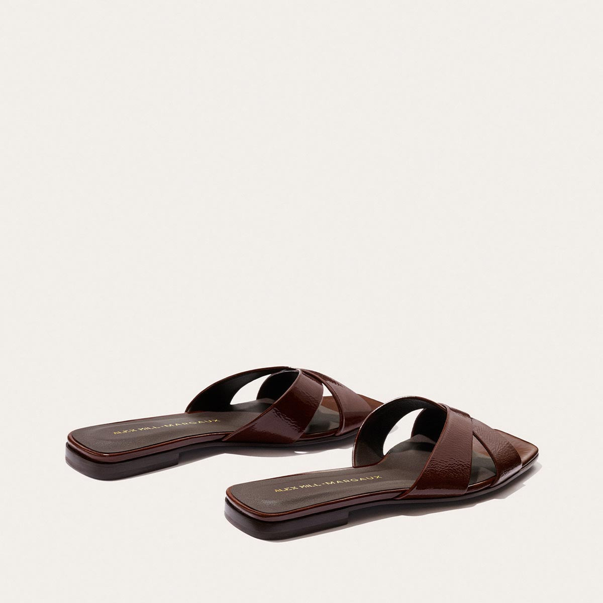 The Alex Mill x Margaux: The Selene Flat Sandal in Espresso Crinkle Patent features crisscross straps and flat soles by Margaux, making it an ideal summer sandal, displayed on a light background.