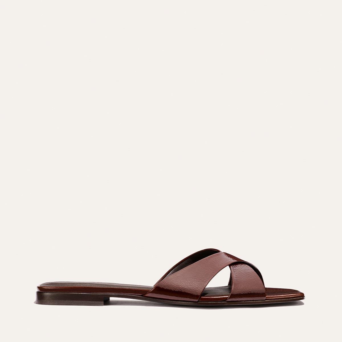 The Alex Mill x Margaux Selene Flat Sandal in Espresso Crinkle Patent features two wide, crisscross straps and a flat sole, shown against a light background—a stylish summer sandal from Margaux.