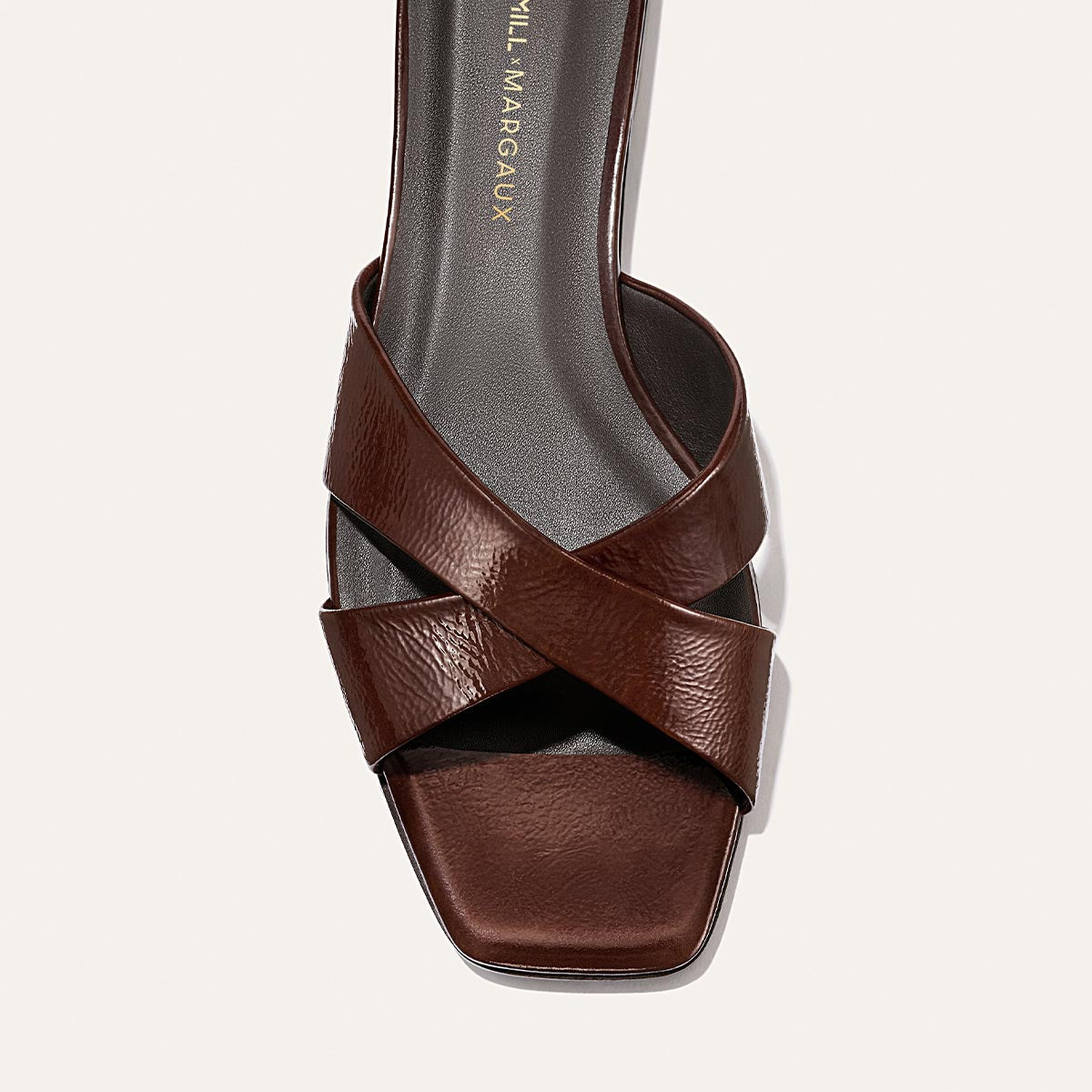 A top view of the Margaux Alex Mill x Margaux: The Selene Flat Sandal in Espresso Crinkle Patent, featuring crisscrossed brown straps, a square toe, black footbed, and gold insole branding—your go-to summer sandal.