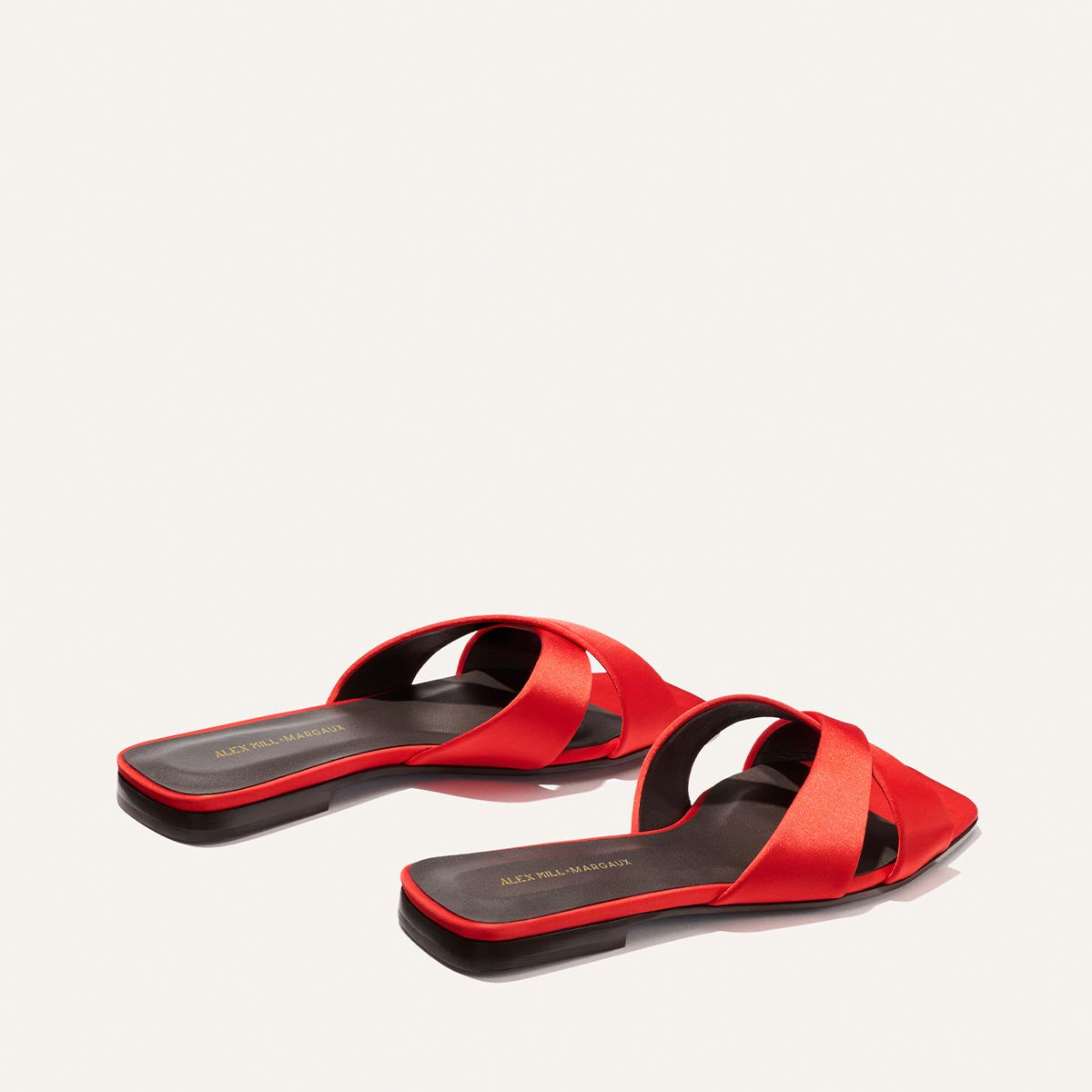 The Alex Mill x Margaux: The Selene Flat Sandal in Poppy Satin by Margaux is a red, open-toe, slip-on sandal with wide crisscross straps and a slight heel, shown on a plain white background.