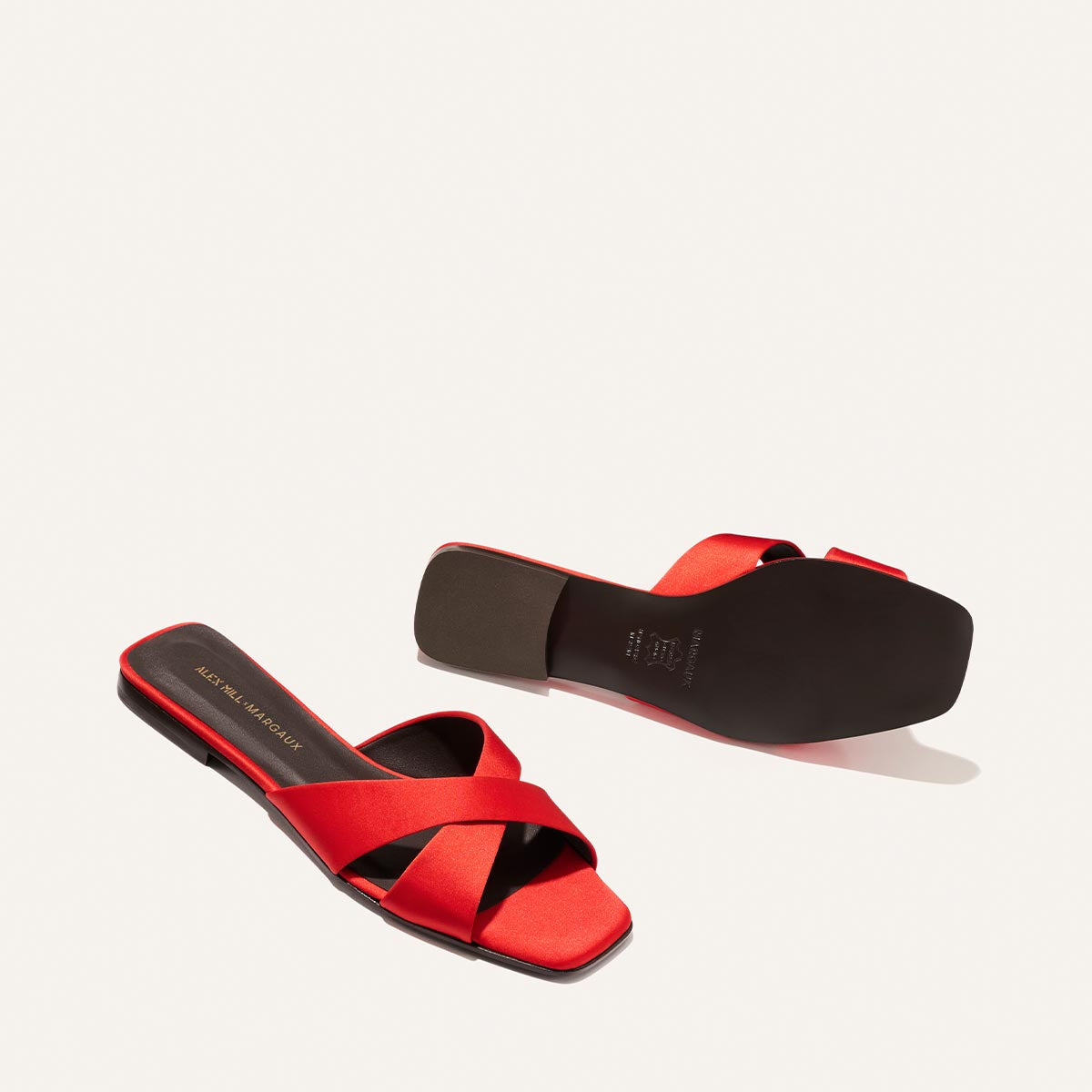 The Alex Mill x Margaux: The Selene Flat Sandal in poppy satin features crisscross straps and flat black soles, shown from top and bottom on a plain light background—ideal summer sandals for casual occasions. Brand: Margaux.