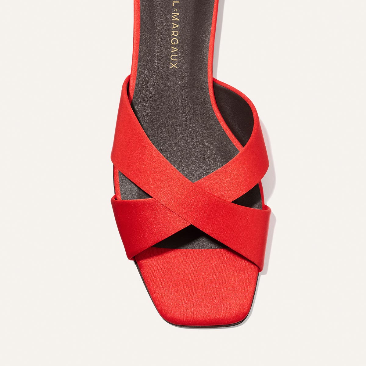 A close-up top view of the Alex Mill x Margaux: The Selene Flat Sandal in poppy satin, a red slip-on with wide crisscross straps, square toe, and dark insole with gold text—perfect summer style from Margaux.