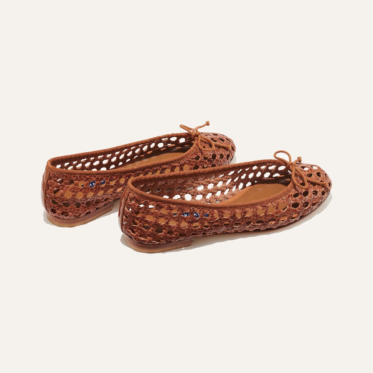 The Demi - Saddle Woven Leather by margaux-development are handmade in Spain, featuring brown woven leather, rounded toes, an open lattice design, and small front bows, shown on a plain light background.